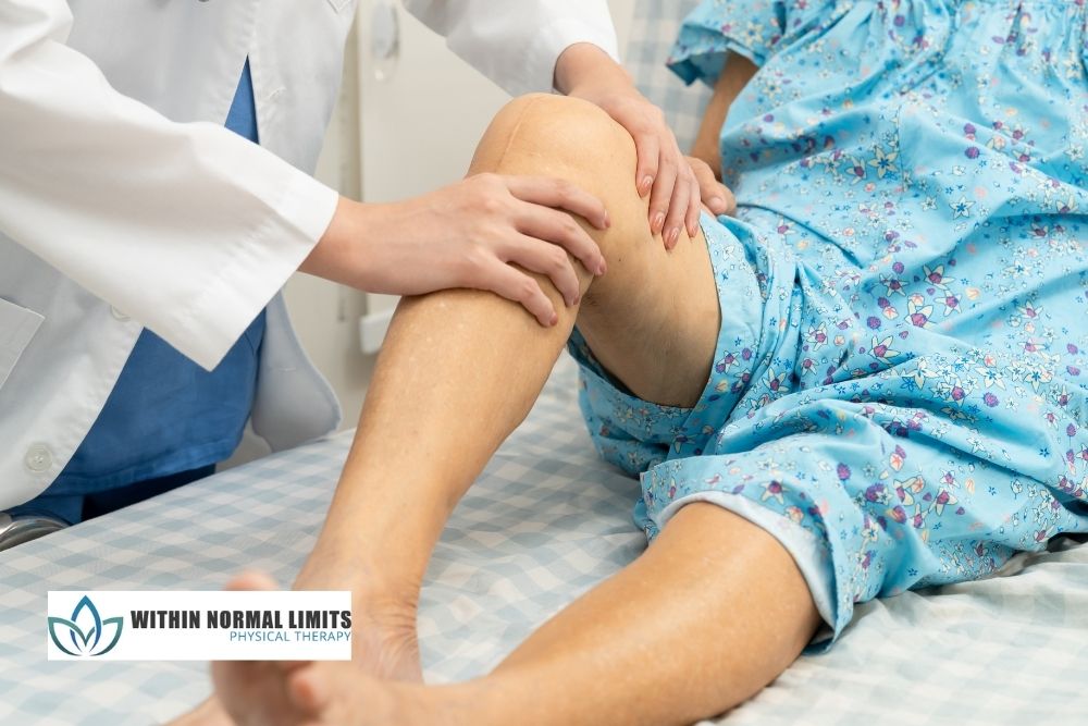 A healthcare professional examines a patient's knee and leg while the patient lies on an exam table, wearing a hospital gown.